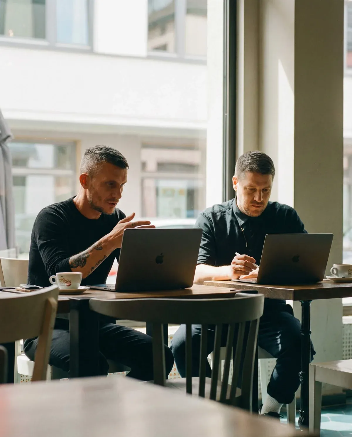 Two recruiters discussing client strategy over laptops in a cafe